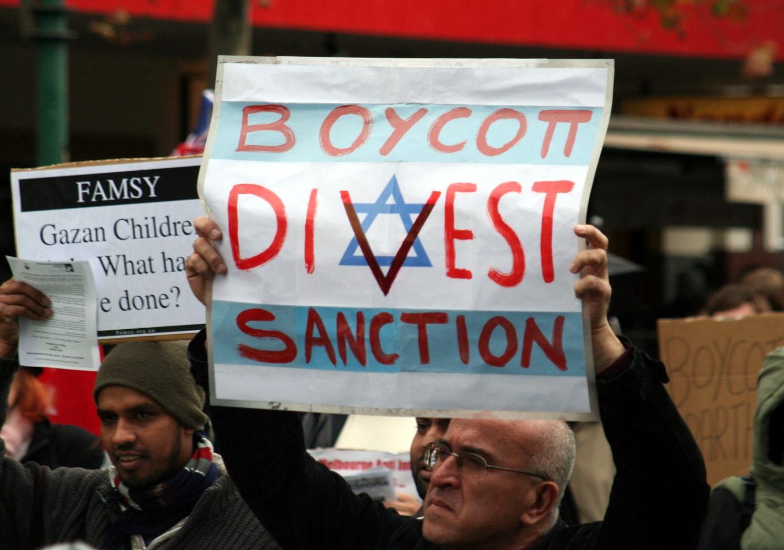 Un signore con in mano un cartellone che invita a “Boycott Divest Sanction Israel"