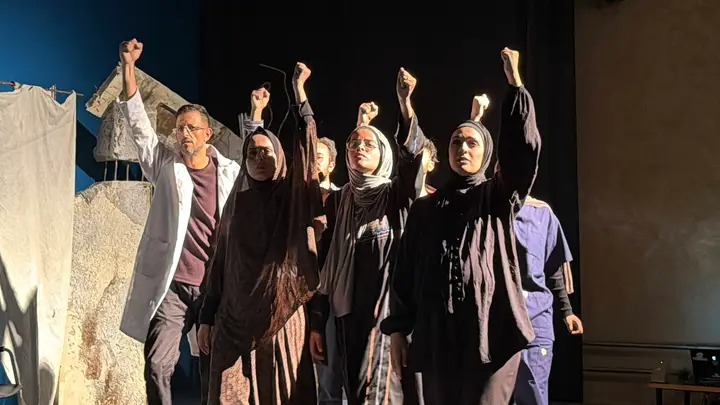 Gli attori nella scena finale, in fila indiana sul palco, con i pugni alzati in segno di speranza e determinazione.