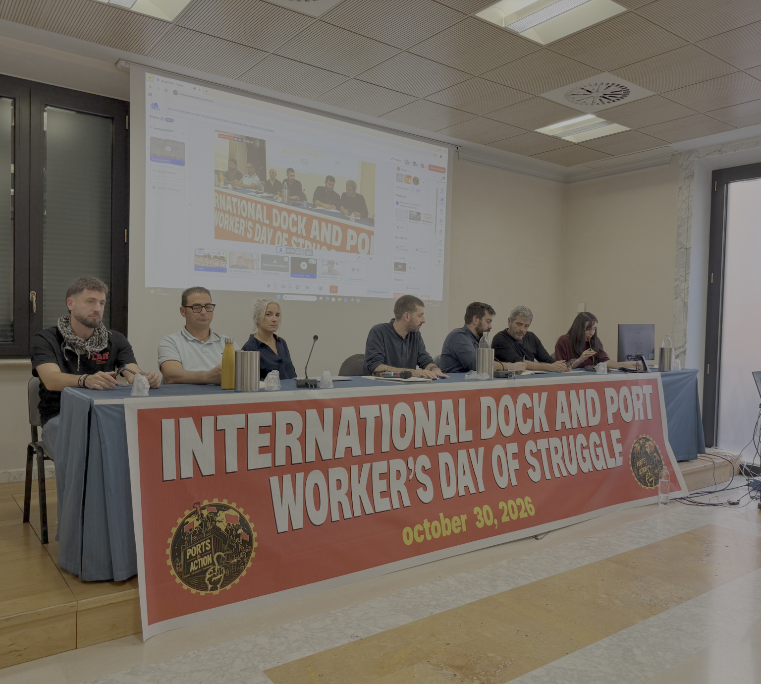 Il tavolo della conferenza stampa a Roma il 15 ottobre scorso con sindacalisti italiani e greci fra gli altri a presentare lo sciopero portuale internazionale del 30 ottobre. Lo striscione sotto recita: "International Dock and Port Worker's Day Struggle".