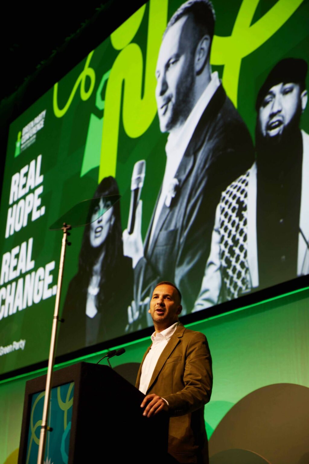 “Il sionismo è razzismo”, la mozione del Green Party britannico, in italiano Zack Polanski sul palco durante il congresso, con sullo sfondo un cartellone dai toni verdi che dice “Real Hope. Real Change."
